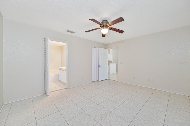 unfurnished bedroom featuring connected bathroom, ceiling fan, light tile patterned flooring, and a textured ceiling