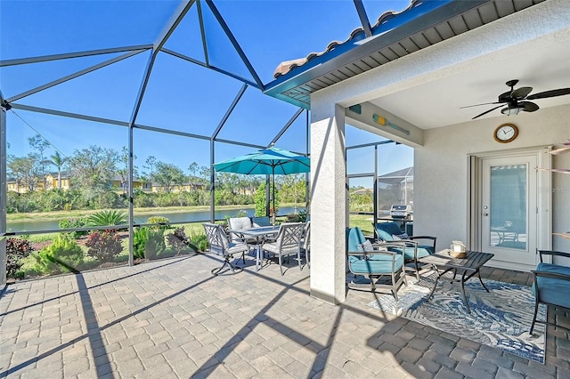 view of patio featuring a water view, glass enclosure, a ceiling fan, and outdoor dining space