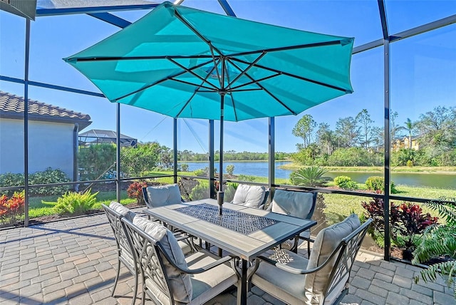 view of patio featuring glass enclosure, outdoor dining space, and a water view