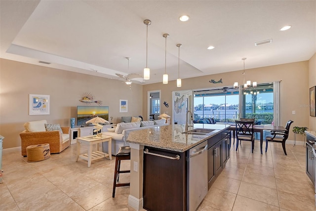 kitchen featuring dishwasher, a center island with sink, ceiling fan with notable chandelier, light stone countertops, and decorative light fixtures