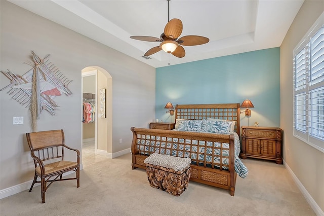 carpeted bedroom with ceiling fan, a raised ceiling, a spacious closet, and multiple windows