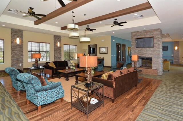 living room with beamed ceiling, hardwood / wood-style flooring, a stone fireplace, and a tray ceiling