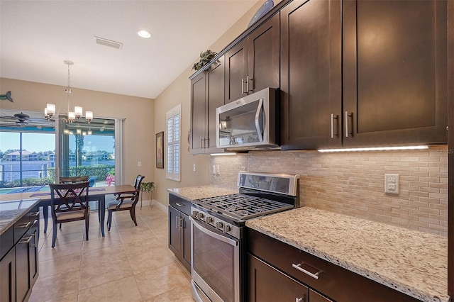 kitchen with light stone countertops, appliances with stainless steel finishes, dark brown cabinets, a chandelier, and hanging light fixtures