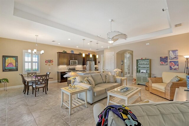 tiled living room featuring ceiling fan with notable chandelier and a raised ceiling