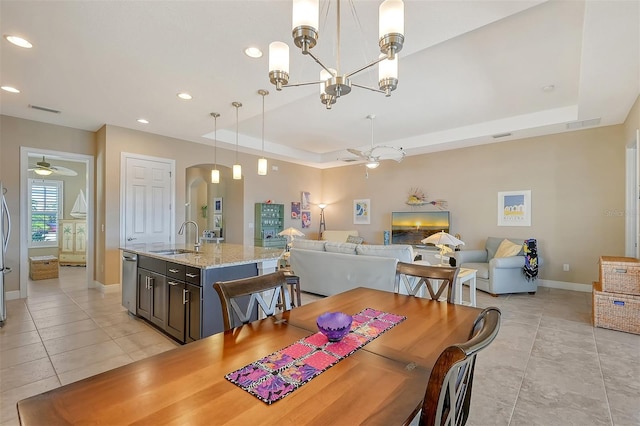 dining space featuring ceiling fan with notable chandelier, light tile patterned floors, sink, and a tray ceiling