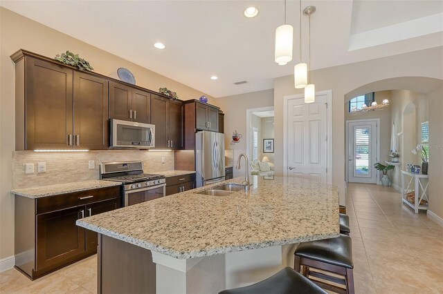 kitchen featuring a kitchen island with sink, hanging light fixtures, sink, dark brown cabinets, and stainless steel appliances