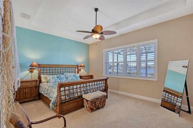 carpeted bedroom with a raised ceiling and ceiling fan