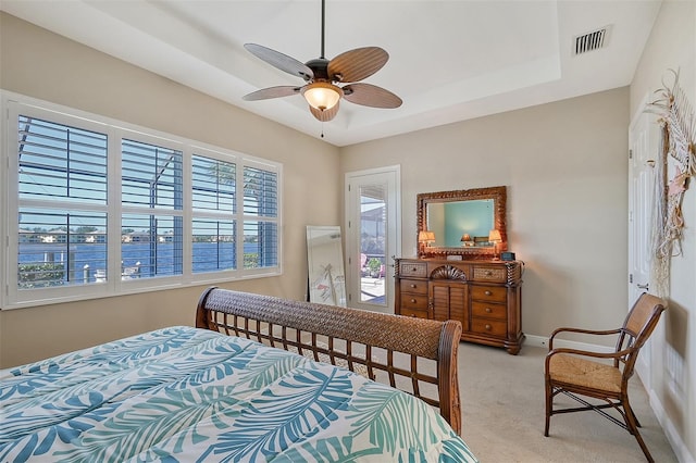 carpeted bedroom with ceiling fan, a tray ceiling, and multiple windows