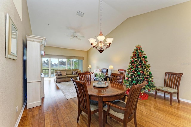 dining space with ceiling fan with notable chandelier, light hardwood / wood-style floors, and lofted ceiling