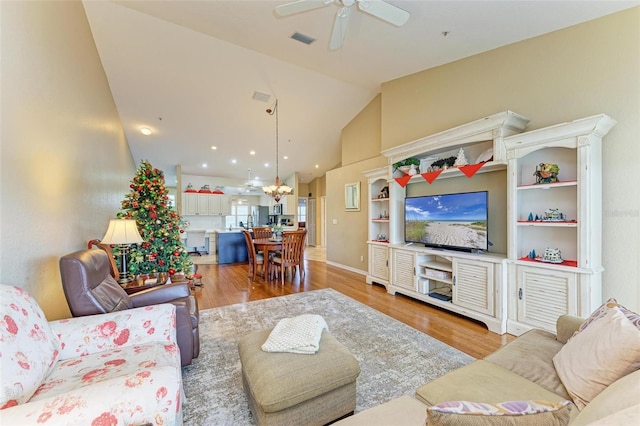 living room featuring lofted ceiling, light wood-type flooring, and ceiling fan with notable chandelier