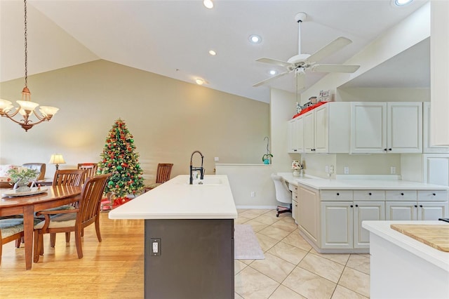 kitchen with white cabinetry, sink, pendant lighting, vaulted ceiling, and ceiling fan with notable chandelier