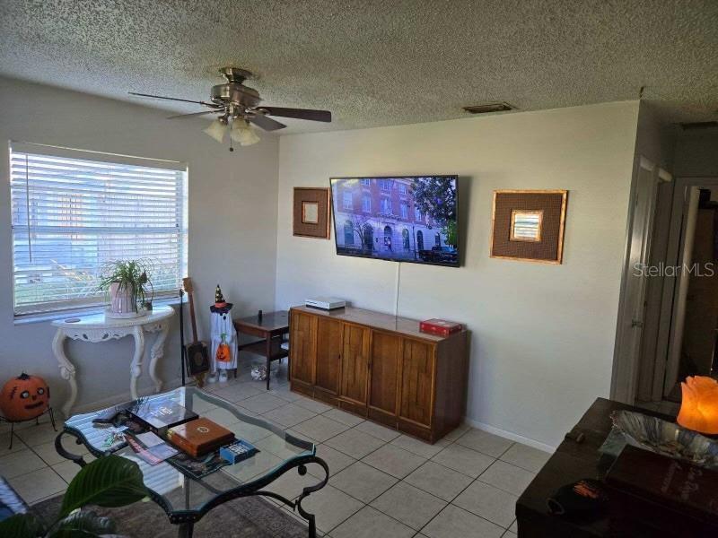 tiled living room with ceiling fan and a textured ceiling