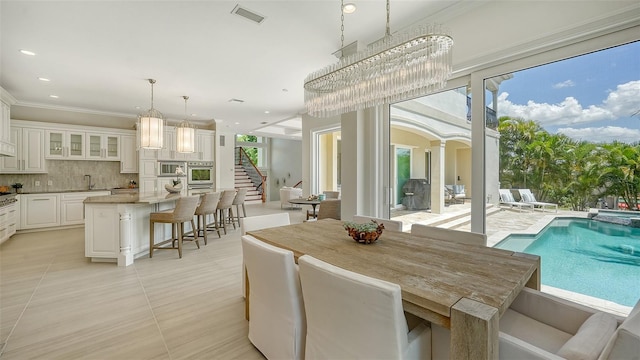 dining space with an inviting chandelier, sink, crown molding, light tile patterned floors, and decorative columns