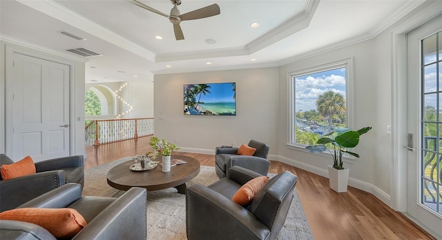 living area with a tray ceiling, ceiling fan, crown molding, and light wood-type flooring