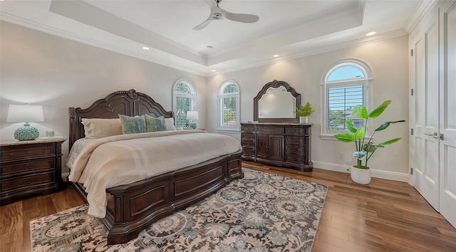 bedroom featuring ornamental molding, hardwood / wood-style flooring, ceiling fan, and a tray ceiling