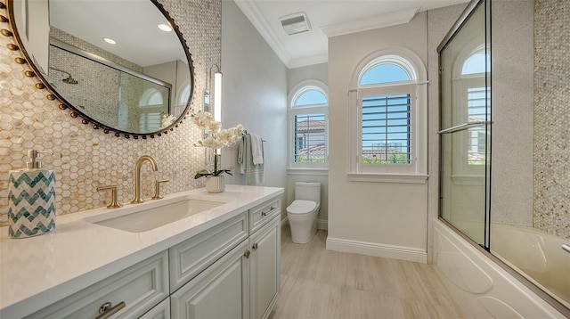 full bathroom featuring vanity, backsplash, combined bath / shower with glass door, crown molding, and toilet