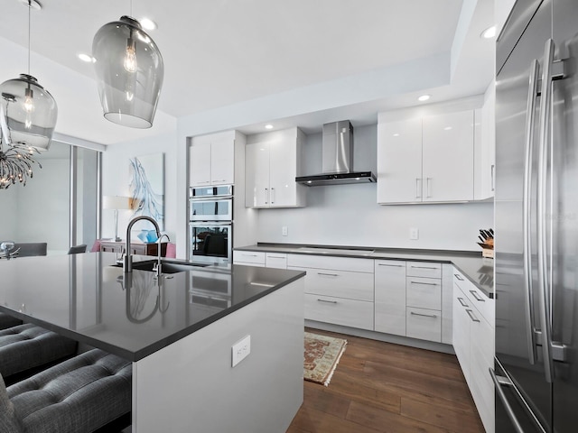 kitchen featuring appliances with stainless steel finishes, dark hardwood / wood-style flooring, wall chimney exhaust hood, a kitchen island with sink, and white cabinetry