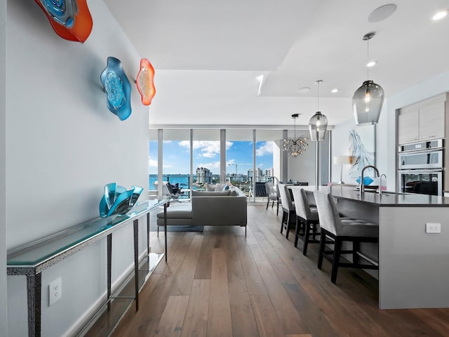 interior space featuring dark hardwood / wood-style flooring, stainless steel double oven, pendant lighting, an inviting chandelier, and a wall of windows