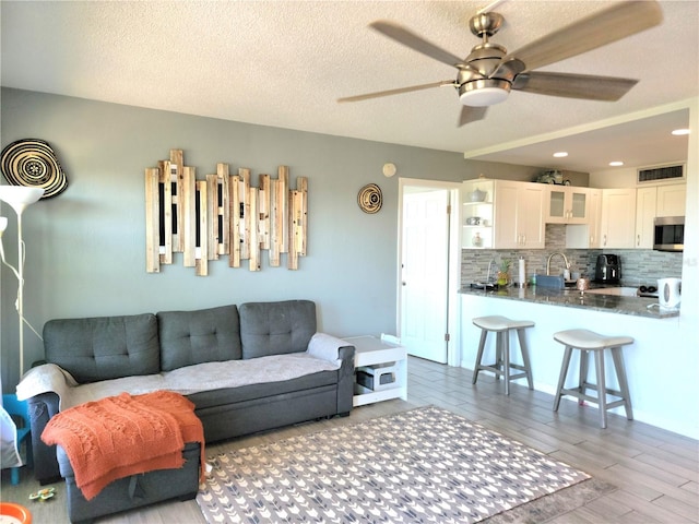 living room with a textured ceiling, light hardwood / wood-style flooring, ceiling fan, and sink