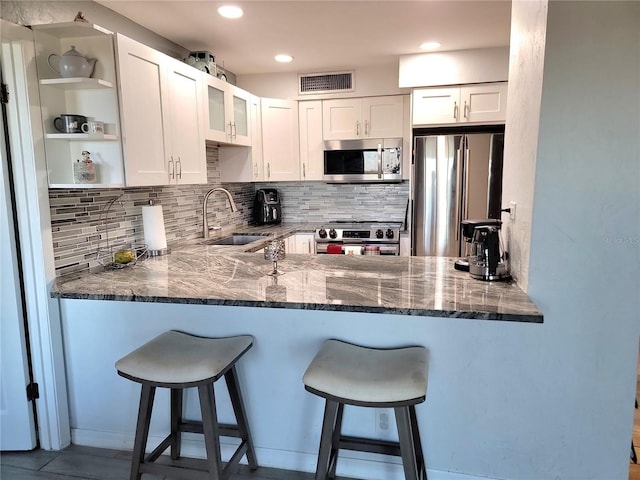 kitchen with white cabinets, sink, dark stone countertops, appliances with stainless steel finishes, and kitchen peninsula