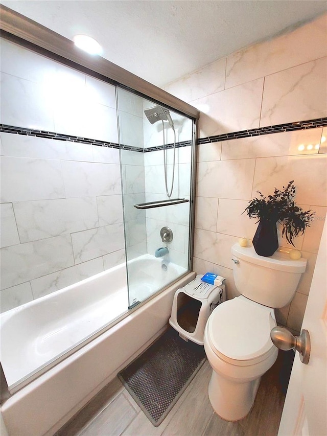 bathroom featuring hardwood / wood-style flooring, toilet, combined bath / shower with glass door, and tile walls