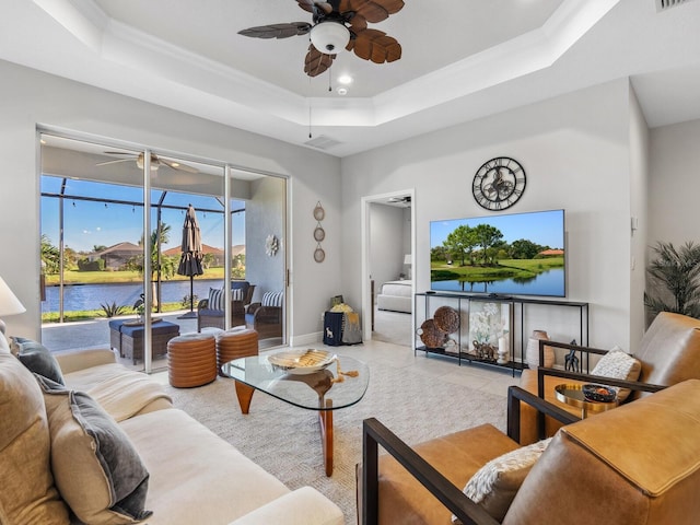 living room with ceiling fan, a water view, and a tray ceiling