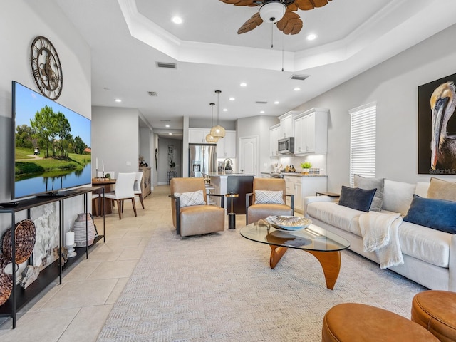 living room featuring ceiling fan, ornamental molding, and a tray ceiling