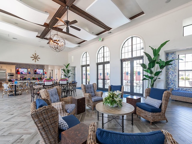 living room with french doors, a towering ceiling, light parquet flooring, ceiling fan with notable chandelier, and ornamental molding