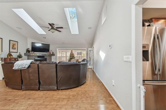 living room featuring ceiling fan, lofted ceiling with skylight, and light wood-type flooring