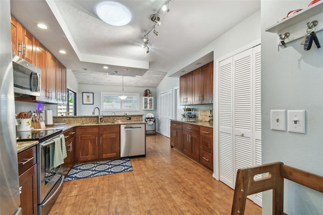 kitchen featuring sink, hanging light fixtures, light stone countertops, appliances with stainless steel finishes, and kitchen peninsula