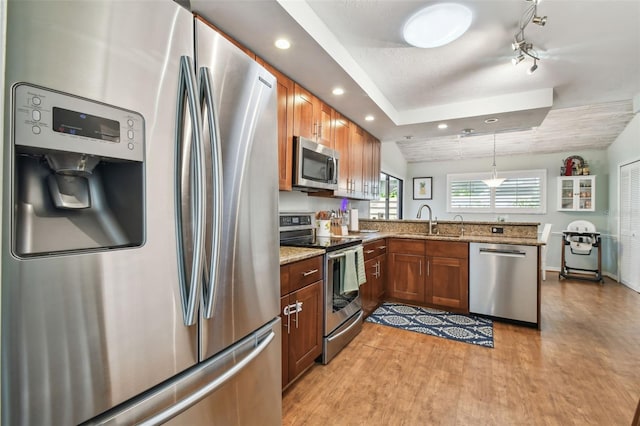 kitchen featuring sink, appliances with stainless steel finishes, decorative light fixtures, light stone counters, and kitchen peninsula