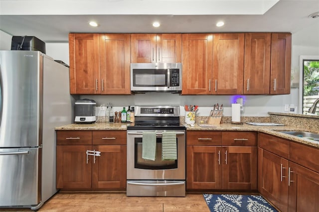 kitchen with light stone countertops, sink, light wood-type flooring, and appliances with stainless steel finishes