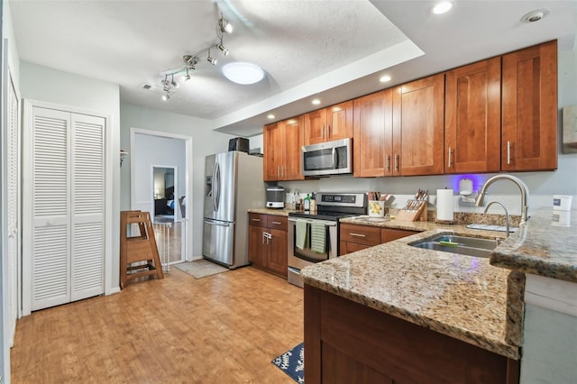 kitchen with light stone counters, sink, appliances with stainless steel finishes, and light hardwood / wood-style flooring