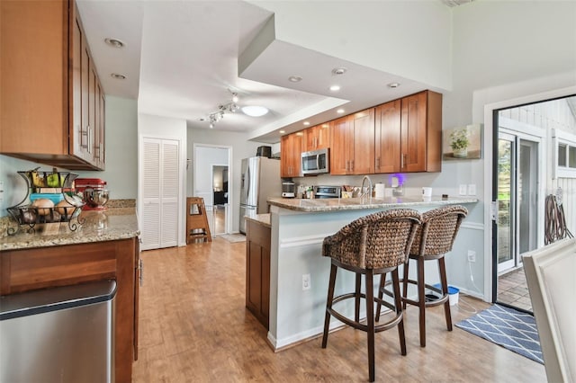 kitchen featuring a breakfast bar area, light wood-type flooring, light stone countertops, kitchen peninsula, and stainless steel appliances