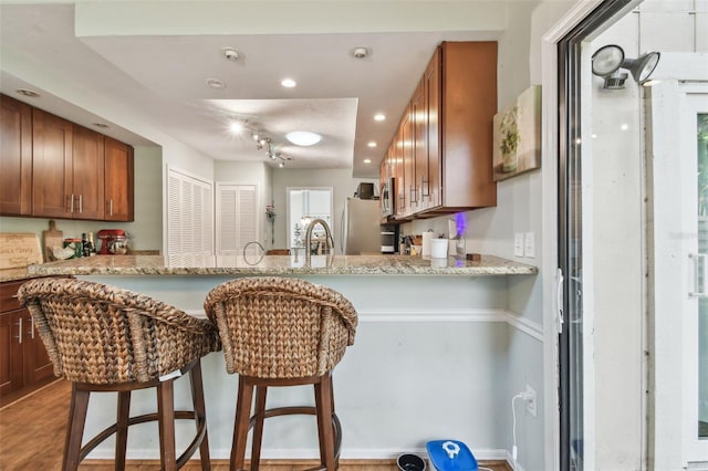 kitchen featuring hardwood / wood-style flooring, light stone countertops, kitchen peninsula, and stainless steel refrigerator