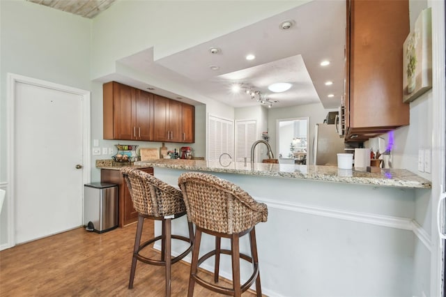 kitchen featuring kitchen peninsula, stainless steel fridge, light hardwood / wood-style floors, and light stone counters