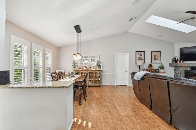 interior space featuring ceiling fan, light stone counters, pendant lighting, vaulted ceiling, and light wood-type flooring