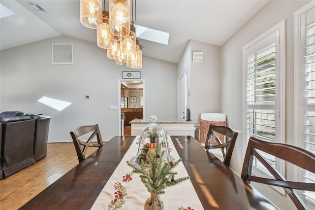 dining room featuring hardwood / wood-style floors, lofted ceiling with skylight, sink, and a chandelier