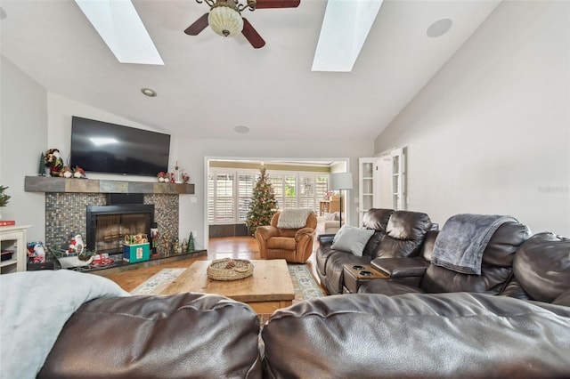 living room featuring ceiling fan, french doors, lofted ceiling with skylight, wood-type flooring, and a tiled fireplace