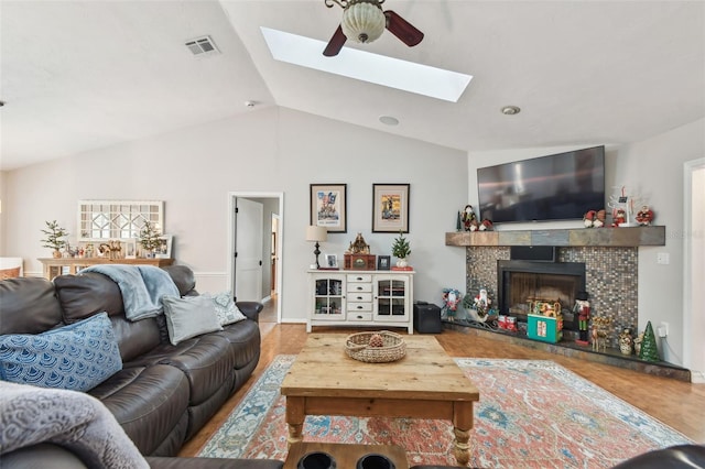 living room featuring hardwood / wood-style floors, ceiling fan, lofted ceiling with skylight, and a fireplace