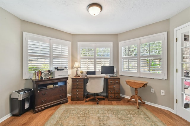 home office with light hardwood / wood-style floors and a textured ceiling