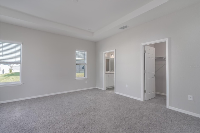 unfurnished bedroom featuring a walk in closet, light carpet, a closet, and ensuite bath