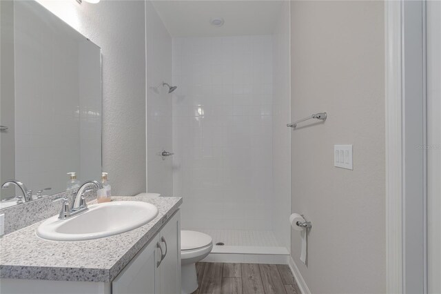 bathroom featuring hardwood / wood-style floors, vanity, toilet, and tiled shower