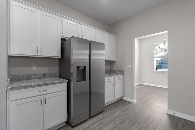 kitchen featuring white cabinets, stainless steel fridge, light wood-type flooring, and light stone counters