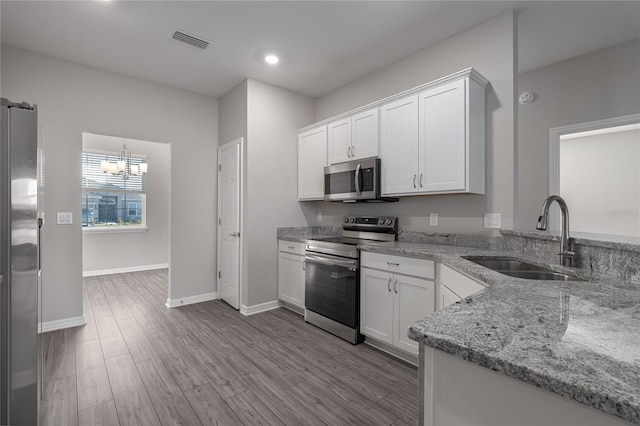 kitchen with light stone counters, stainless steel appliances, sink, a chandelier, and white cabinetry