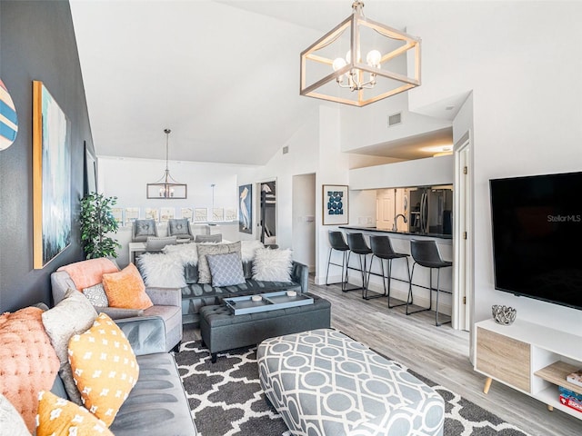 living room featuring wood-type flooring, high vaulted ceiling, a notable chandelier, and sink