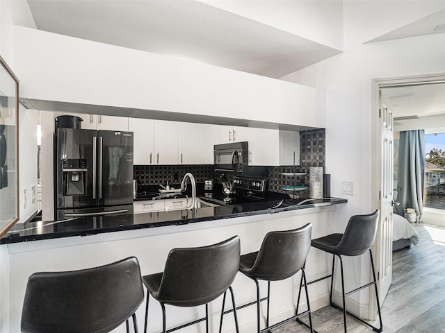 kitchen featuring white cabinetry, tasteful backsplash, kitchen peninsula, black appliances, and light wood-type flooring