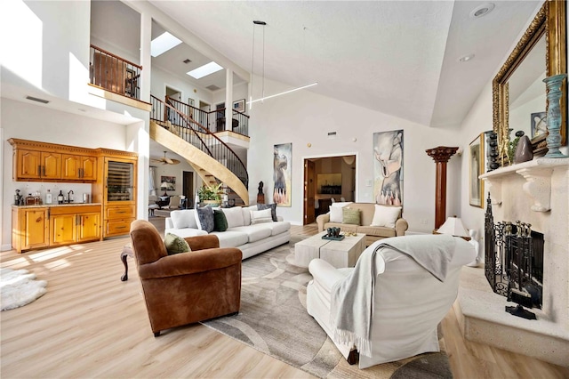 living room featuring ceiling fan, light wood-type flooring, high vaulted ceiling, and a skylight