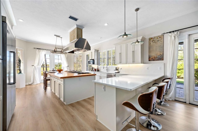 kitchen featuring hanging light fixtures, kitchen peninsula, light hardwood / wood-style floors, island range hood, and white cabinets