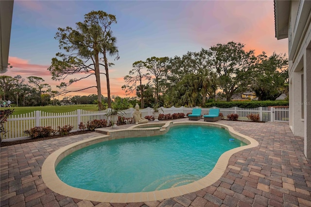 pool at dusk featuring an in ground hot tub and a patio